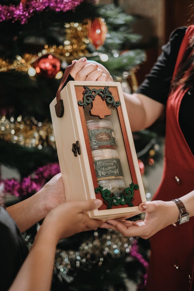 A wooden gift box held up beside a Christmas tree
